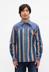 Ένα πολύχρωμο υφασμάτινο π ουκάμισο με κατακόρυφες ρίγες σε μπλε, ροζ, κίτρινο και πράσινο. Γιακάς και μανίκια σε στυλ τζιν με κούμπωμα με κουμπιά snap.