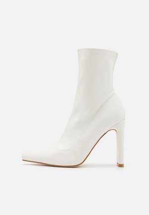 Weißer Stiefelette mit hohem Absatz, spitzer Vorderkappe, glatter Oberfläche und schlankem Stilettabsatz, in Seitenansicht vor einfarbigem Hintergrund gezeigt.