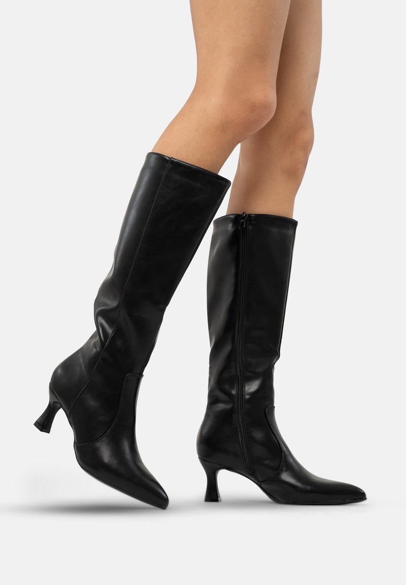 Botas negras hasta la rodilla con un diseño ajustado, material de cuero suave, punta afilada y un tacón de 7,5 cm. Incluyen una cremallera lateral para el cierre.