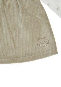 Helles beige Cord-Rippenrock mit vertikalen Rippungen und einem gestickten Katzenkopf nahe dem Saum. Der Stoff hat eine weiche Textur und das Design weist einfache Nähte auf.