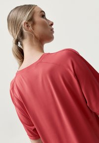 Červený krátký rukáv s hladkým, lehkým materiálem a širokým výstřihem, který má uvolněný střih a jemné ramenní švy.