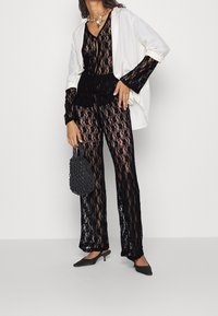 Ensemble comprenant un haut en dentelle noire et un pantalon, superposé avec une veste blanche ample. Présente un tissu texturé et une silhouette ajustée, complété par des accessoires noirs.