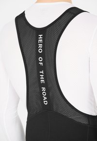 Cuissards de cyclisme noirs avec un panneau arrière en mesh comportant le texte "HÉROS DE LA ROUTE". Tissu lisse avec un design ajusté pour le confort.