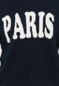 Námornícky sveter s hrubým bielym nápisom "PARÍŽ". Mäkká textúra, rebrovaný dizajn a okrúhly výstrih. Jednoduchý a výrazný vizuálny prvok.