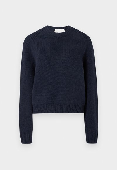 Tumši zils adīts džemperis ar apaļu kaklu, garām piedurknēm, ribotām aprocēm un apakšu. Raksturīgs strukturēts apdare un smalkas plecu detaļas.