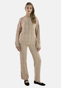 Beige knitted sweater and pants set featuring a cable knit pattern, relaxed fit, and long sleeves; paired with black flats.