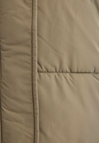 Beige Steppjackenstoff mit glatter Textur und gesteppten Abschnitten, mit einer Naht auf der linken Seite und einem dezenten Schimmer.