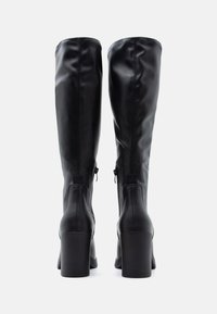 Black knee-high boots made of smooth leather, featuring a chunky heel, side zippers, and stitched accents. Back view shows boot contouring.