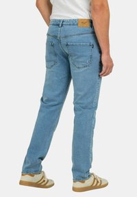 Jeans de mezclilla azul claro con pierna recta, que cuentan con bolsillos traseros y una etiqueta de cuero en la cinturilla. Complementados con zapatillas blancas y marrones.