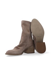 Bottines en daim beige avec un design perforé, une ligne supérieure courbée et un talon empilé. La semelle est plate avec une adhérence texturée et une étiquette "FABRIQUÉ EN ITALIE".