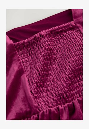 Fuksiaroosa kleit, millel on tekstureeritud smokk büstis, siidine kangas ja volangidega ääred, näidates üles rikkalikku, sügavat värvi ja pehmet sära.