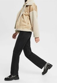 Chaqueta beige y crema con una textura suave y peluda, combinada con pantalones negros de pierna recta y zapatos negros brillantes. Costuras detalladas en la chaqueta.
