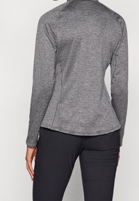 Långärmad sporttop i heathergrått tyg, med en figurnära passform, platta sömmar och hög halsringning. Matchas med svarta leggings.