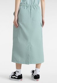 Mint green long skirt made of lightweight fabric, featuring an elastic waistband, two back pockets, and side slits for ease of movement.