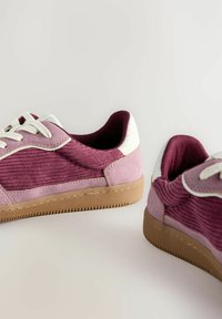 Bordó kordbársony sneaker fehér sarkaival, világos rózsaszín velúr díszítéssel és barna gumitalppal. Fehér fűzővel és texturált felülettel rendelkezik.