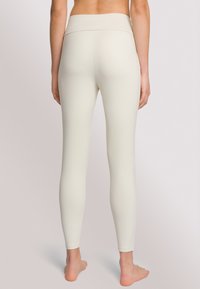 Leggings a vita alta in crema chiaro, realizzati in tessuto elasticizzato con una superficie liscia e senza cuciture visibili, progettati per il comfort e il movimento.