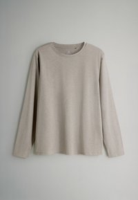 Ilgų rankovių šviesiai béžinė marškinė, pagaminti iš minkštos medžiagos. Turi apvalią iškirptę ir laisvą siluetą, be matomų raštų ar akcentų.