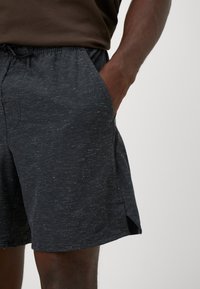 Calças de desporto pretas em tecido texturizado, com cintura elástica e bolsos laterais. Apresentam um padrão heather subtil e fendas laterais para maior flexibilidade.