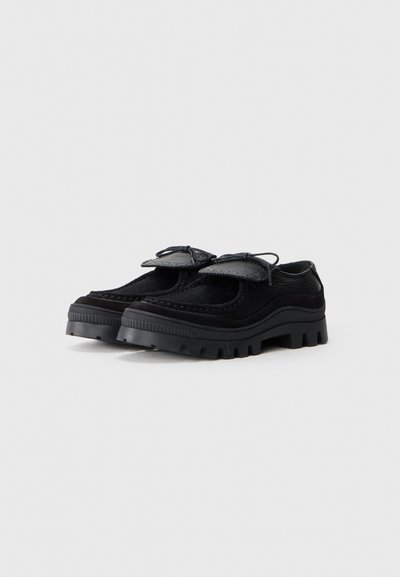 Black shoes featuring a combination of smooth leather and textured material, with a rugged sole and decorative bow accents on the front.