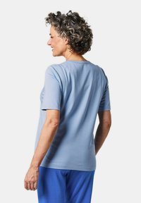 Lichtblauw T-shirt met korte mouwen en een ronde halslijn, gemaakt van zachte stof, getoond vanaf de achterkant, gecombineerd met blauwe broek.