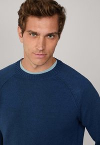 Námornícka modrý pletený sveter s rebrovaným okrúhlym výstrihom a raglánovými rukávmi, s jemnou textúrou a subtílnymi detailmi v látke.
