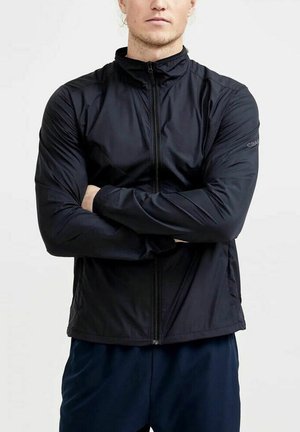Schwarze leichte Jacke mit hohem Kragen, Reißverschluss, glatter Textur, schlanker Passform und dezentem Branding am Ärmel.