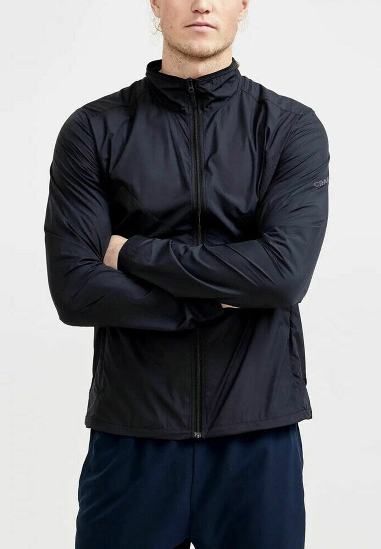 Schwarze leichte Jacke mit hohem Kragen, Reißverschluss, glatter Textur, schlanker Passform und dezentem Branding am Ärmel.