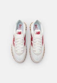 Vita och röda New Balance-sneakers med gummisulor, ovanifrån, snörda, placerade sida vid sida på en vit bakgrund.