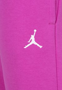 Rozā kokvilnas sporta bikses ar baltu Jumpman logo, kas apdrukāts kreisajā augšstilbā, ar gludu tekstūru un ikdienišķu dizainu.