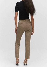 Pantalon écossais marron près du corps avec une texture lisse et deux poches arrière, associé à un haut noir à manches courtes et des sandales argentées.