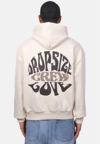 Hoodie in hellbeige mit einem großen Rückendruck in Schwarz und Grau, der die Worte "DROPSIZE CREW LOVE" in verspielten Schriftarten zeigt.