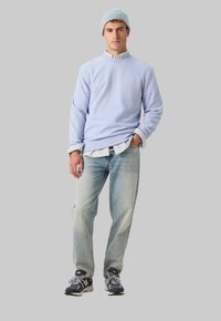 Sweatshirt bleu clair avec col haut, superposé à une chemise rayée blanche, associé à un jean en denim délavé et des baskets foncées.