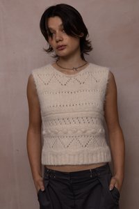 Krémový pletený bezrukávový top s texturovaným vzorem, který obsahuje vyvýšené tečky a geometrické designy, zakončený žebrovaným lemem.