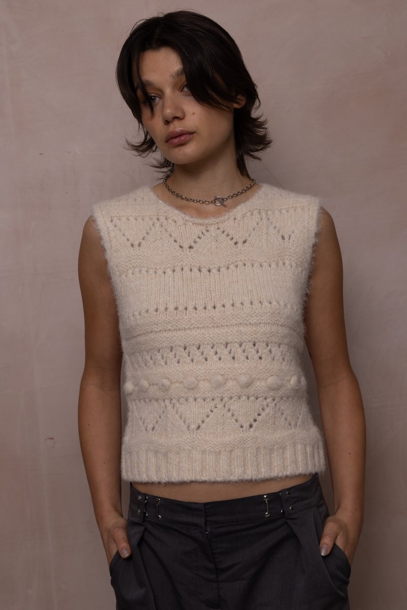 Krémový pletený bezrukávový top s texturovaným vzorem, který obsahuje vyvýšené tečky a geometrické designy, zakončený žebrovaným lemem.
