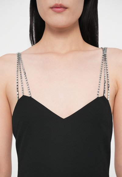 Rochie neagră cu decolteu în V, cu bretele argintii asemănătoare lanțurilor. Materialul este neted, fără modele sau texturi vizibile.