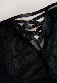 Black lace fabric featuring floral patterns and decorative black straps connected by small gold rings.