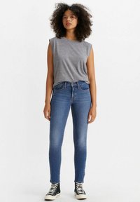 Top gris sin mangas combinado con unos vaqueros de denim azul ajustados. Los vaqueros tienen un diseño clásico de cinco bolsillos y se llevan con unas zapatillas de caña alta.