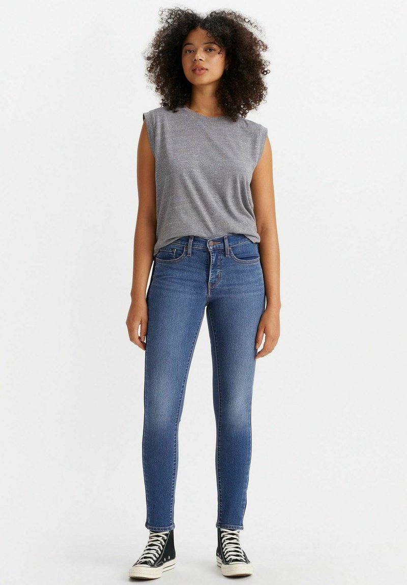 Top gris sin mangas combinado con unos vaqueros de denim azul ajustados. Los vaqueros tienen un diseño clásico de cinco bolsillos y se llevan con unas zapatillas de caña alta.