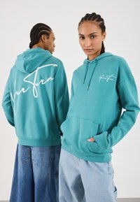 Sudadera con capucha en color turquesa con un bolsillo frontal; presenta un logotipo en escritura blanca en la parte delantera y trasera; fabricada en tela suave; corte holgado.