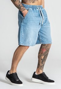 Pantalones cortos de mezclilla azul claro con cintura elástica y cordón, con bolsillos laterales; combinados con zapatillas negras con detalles brillantes.