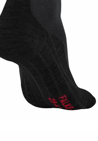 Czarna skarpetka z prążkowaną teksturą i wzmocnioną piętą. Czerwone logo jest wyraźnie widoczne z boku, służąc jako element markowy.