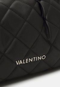 Borsa in pelle nera trapuntata con logo metallico "Valentino" e una texture leggermente arricciata su un lato. Finitura liscia con cuciture visibili.