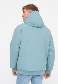 Lys blå hættejakke med en glat, tekstureret finish. Har ribbede manchetter og kant, samt et logo på ærmet. Bagfra.
