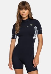 Combinaison de plongée à manches courtes en bleu marine, avec des panneaux latéraux à motifs, des coutures à plat et des accents de logo sur la poitrine et la manche.