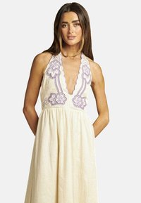 Cremfarbendes Halterkleid mit lila floralem Stickereimuster, gewelltem Ausschnitt und schwingendem Rock. Hergestellt aus leichtem Stoff mit einer weichen Textur.