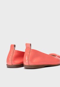 Bailarinas de cuero coral con un acabado suave, punta redonda y tacón bajo. Presentan un diseño elegante y minimalista con una trabilla en la parte trasera.