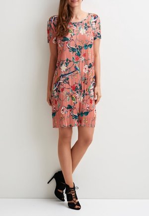 Pehmeän vaaleanpunainen kukkakuvioinen mekko, jossa on lyhyet hihat, laskosmainen tekstuuri ja suora leikkaus. Yhdistetty mustiin nauhakorollisiin korkokenkiin.