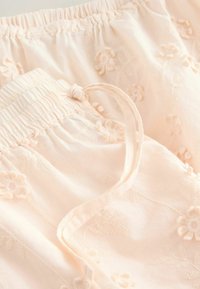 Ljust rosa pyjamasbyxor i mjukt tyg, med blommönsterbroderier och en samlad elastisk midja med dragsko.