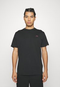 Black cotton t-shirt with a round neckline and short sleeves. Features a small pink logo on the left chest and is paired with black pants.