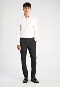 Biała koszula zapinana na guziki w połączeniu z czarnymi, dopasowanymi spodniami i czarnymi butami wizytowymi. Koszula ma klasyczny kołnierzyk oraz dopasowany krój.